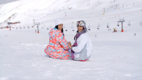 Two-young-women-sitting-in-snow-at-a-ski-resort