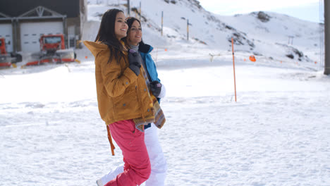Two-young-women-walking-through-snow-at-a-resort