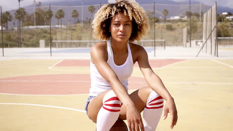 Blond-smiling-female-athlete-sits-on-basketball