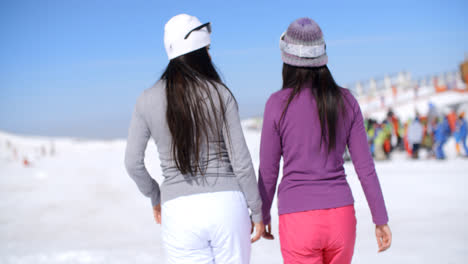 Dos-Mujeres-Jóvenes-Caminando-En-Una-Estación-De-Esquí-De-Invierno