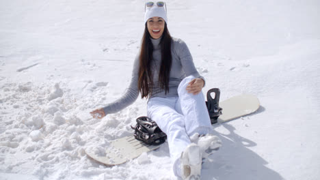 Atractiva-Mujer-Joven-Sentada-En-Su-Tabla-De-Snowboard