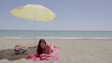 Woman-on-phone-call-at-beach-under-umbrella