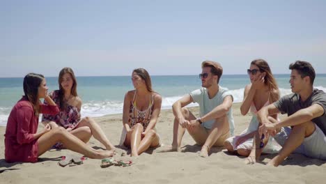 Group-of-six-friends-sitting-in-sand-on-beach