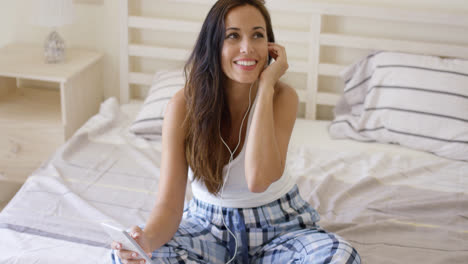 Laughing-woman-using-device-with-ear-buds-in-bed