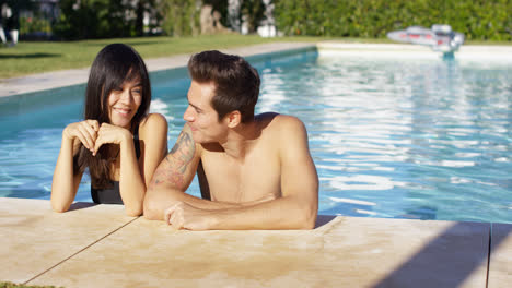 Man-in-pool-standing-with-girlfriend-kisses-her