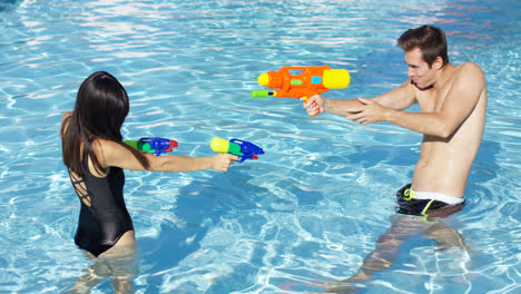 Glückliches-Paar,-Das-Wasserpistolen-Im-Pool-Abschießt