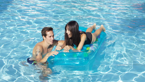 Glückliches-Junges-Paar,-Das-Auf-Einer-Matratze-Im-Pool-Schwimmt