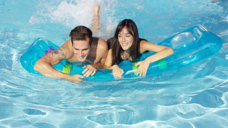 Joyful-couple-swimming-together-on-floatie-in-pool