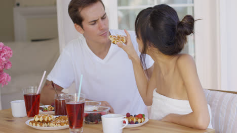 Woman-trying-to-feed-annoyed-man-a-waffle