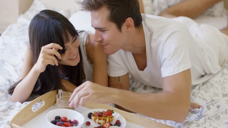 Couple-having-fruit-and-waffle-breakfast-in-bed
