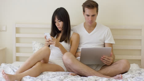 Young-mixed-couple-sitting-in-bed-with-laptop
