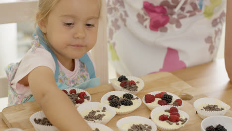 Cute-little-girl-putting-berries-on-muffins