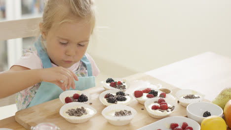 Girl-putting-berries-on-muffins-on-table