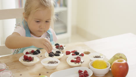 Girl-putting-berries-on-muffins-on-table
