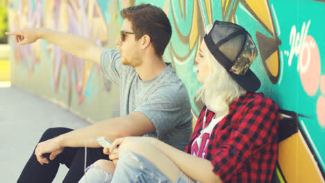 Hipster-couple-relaxing-against-a-graffiti-wall