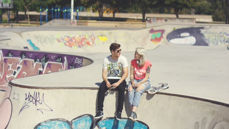 Young-couple-sitting-on-a-wall-at-a-skate-park