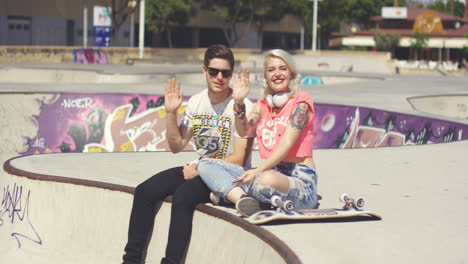 Happy-trendy-young-couple-waving-at-the-camera