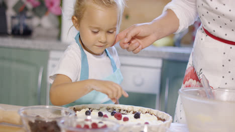 Smiling-little-girl-adding-berries-to-a-pie