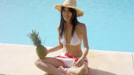 Woman-with-pineapple-and-straw-hat-sits-by-pool
