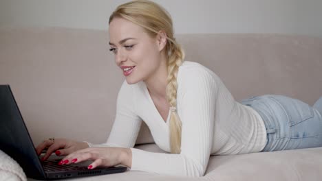Blond-female-lying-on-sofa-and-browsing-laptop