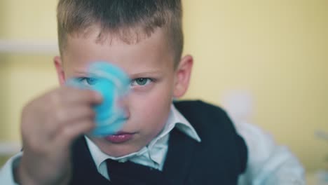 blue-eyed-boy-holds-spinner-resting-in-light-classroom