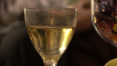 A-medium-shot-of-a-glass-of-sparkling-white-wine-with-a-Christmas-party-reflected-in-it