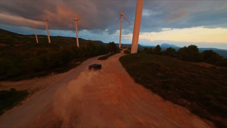 FPV-aerial-following-a-Hummer-driving-through-a-wind-turbine-farm-at-sunset