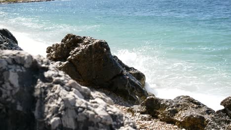Rocky-beach-on-Corfu-Island-with-foamy-waves-crashing-into-a-cliff