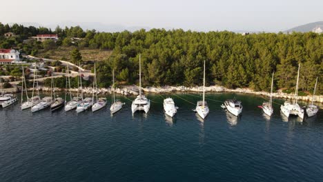 Row-of-sailboats-docked-at-harbor-Fiskardo,-Greece,-aerial-sideways-establisher