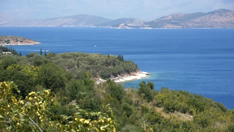 View-of-forested-rocky-cliffs-on-Corfu-Island,-with-the-blue-sea-and-tall-mountains-in-the-background