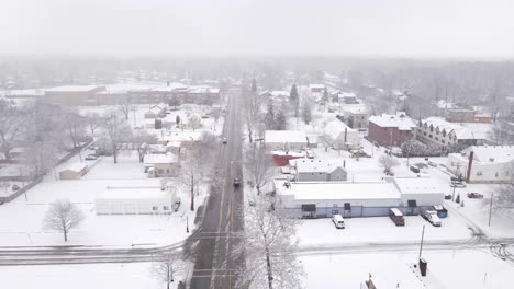 Car-passing-small-American-town-in-winter-season,-aerial-drone-view