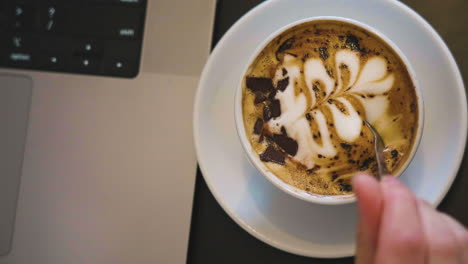 Slow-motion-shot-of-coffee-art-being-stirred-into-the-freshly-made-coffee-at-a-computer