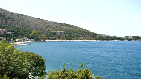 Blick-Auf-Den-Strand-Der-Insel-Korfu,-Das-Blaue-Meer-Und-Die-Berge-Im-Hintergrund