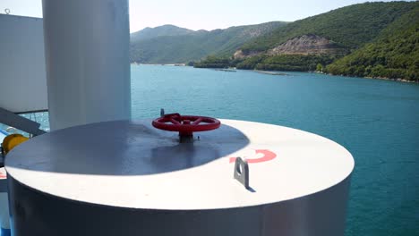Ferry-sailing-along-the-coast-of-Greece-with-a-red-valve,-part-of-its-equipment