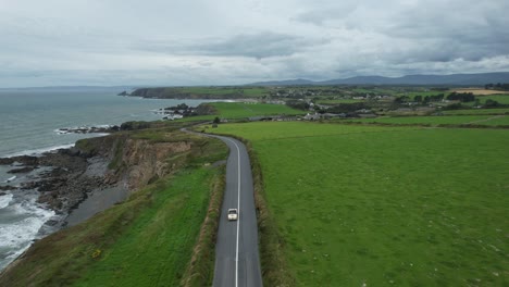 Historic-vintage-rally-car-driving-on-the-classic-Copper-Coast-Drive-Road-in-Waterford-Ireland-stunning-views-of-the-sea-and-Comeragh-Mountains-on-a-fine-summer-morning