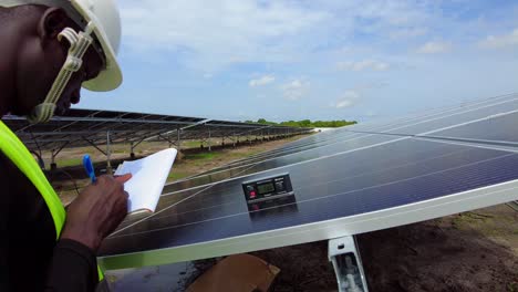 Schwarzer-Männlicher-Professioneller-Ingenieur-Techniker,-Der-An-Der-Solarpanel-Photovoltaikanlage-Eines-Bauernhofs-Für-Erneuerbare-Energien-Arbeitet,-Der-Den-Neigungswinkel-überprüft-Und-Die-Effizienz-In-Afrika-Testet