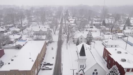 Downtown-of-small-town-in-USA-during-snowfall,-aerial-ascend-view