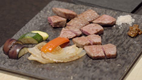 Japanese-kobe-Wagyu-meat-plate-serving-with-slices-of-eggplant-peppers-onion-zucchini-salt-pepper-on-stone-traditional-plate-Japan-restaurant