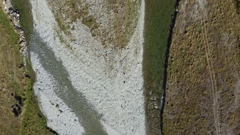 Aerial-view-above-clear-braided-river-with-four-wheel-drive-track-next-to-the-river