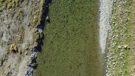 Aerial-view-above-clear-river-flowing-over-gravel-bed-with-grassy-banks