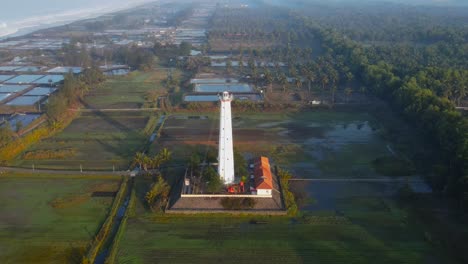 Aerial-view-of-white-lighthouse-surrounded-by-plantation-and-trees