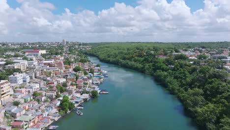 Aerial-flight-over-Rio-Romana-River-with-city-of-Romana-during-sunny-day---Building-on-on-side-and-forest-on-the-other-shoreline