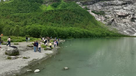 Group-of-tourists-taking-photographs-and-admiring-Boyabreen-glacier-in-Fjaerland-Norway---Crowd-standing-close-to-the-edge-of-green-melted-glacial-water