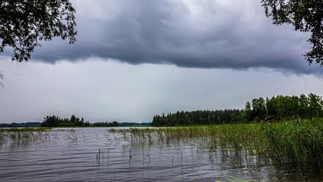 Flowing-clouds-over-a-lake-and-forest-on-a-gray,-overcast-day---time-lapse-cloudscape