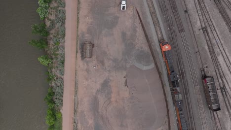 Aerial-top-down-view-of-train-passing-industrial-area-by-river-in-Denver,-Colorado