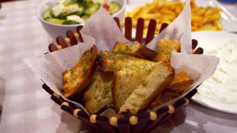 Garlic-seasoned-croutons-lying-in-a-stylish-basket,-with-Greek-salad-in-the-background