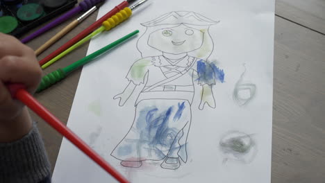 A-mid-shot-of-a-young-child-colouring-in-a-female-figure-with-watercolours,-sat-at-a-desk