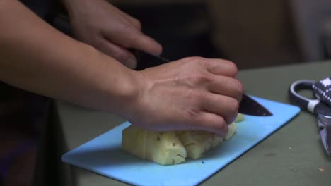 Pineapple-being-cut-by-knife-into-bite-size-pieces-on-blue-chopping-board,-filmed-as-close-up-shot