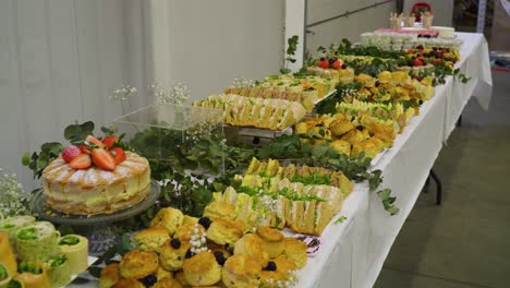 Table-full-of-food-at-business-event-organised-inside-of-warehouse-white-walls-leaves-plant-placed-on-table-as-decoration-moving-backwards-revealing-all-the-sandwiches-sweets-and-rolls