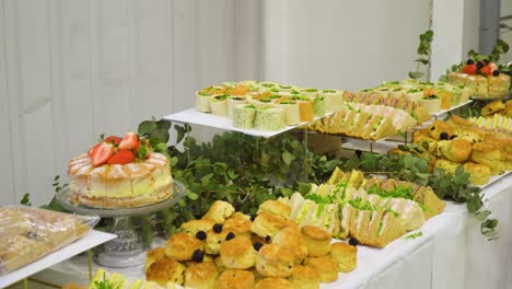 English-buffet-full-of-sandwiches-and-cakes-on-a-long-table-inside-a-warehouse-environment-for-a-business-meeting-moving-sideways-revealing-the-foods-and-selection-offered-for-the-event